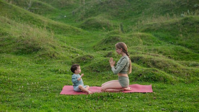 Caucasian woman doing yoga with her little son outdoors. 