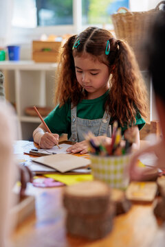 Girl with pigtails drawing at a table.