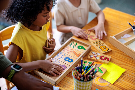 Children learn math with wooden number puzzles and pencils.