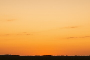 Obraz premium Vibrant Sunset Sky with Warm Orange and Yellow Tones Over a Silhouetted Horizon