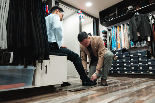 Vendor helping client try on formal shoes in store
