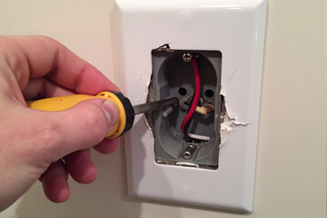 Electrician's hand using a non-contact voltage tester to safely check for live power in the exposed wires of a damaged wall outlet