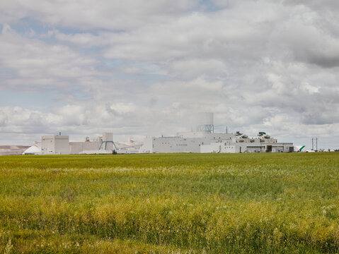 Potash plant beyond prairie field under cloudy sky