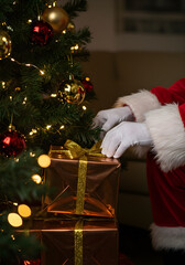 Santa Claus carefully placing a wrapped gift under a decorated Christmas tree, close-up on his gloved hand