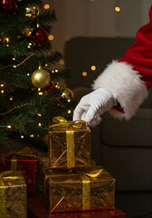 Santa Claus carefully placing a wrapped gift under a decorated Christmas tree, close-up on his gloved hand