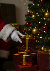 Santa Claus carefully placing a wrapped gift under a decorated Christmas tree, close-up on his gloved hand