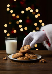 Close-up of Santa’s gloved hand reaching for a plate of chocolate chip cookies and a glass of milk on a table, cookie crumbs visible, soft warm lights, shallow depth of field - 1