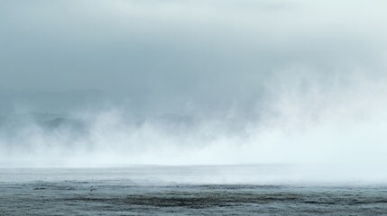 Fototapeta premium A misty landscape with soft gray tones, featuring low-lying fog covering the ground and distant hills, creating an ethereal and serene atmosphere.