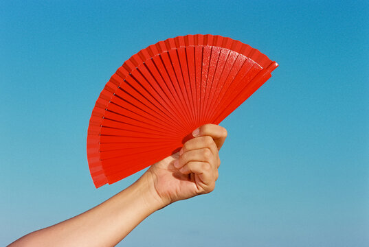 a man raises a red hand fan under a cloudless sky, 35mm film