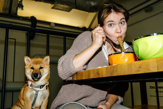 Woman eating noodles while puppy sitting beside her at cafe table