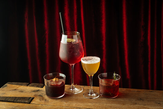 ssorted colorful cocktails on wooden table against red curtain