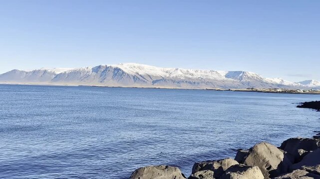 Scenic view of Reykjav&iacute;k, Iceland, featuring Mount Esja and Faxafl&oacute;i Bay, where the city meets icy mountains and the calm sea, capturing the serene beauty of urban life surrounded by nature.