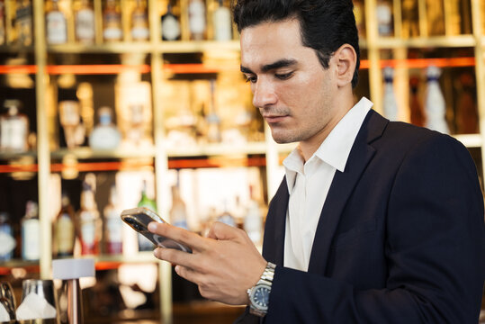 Confident young businessman checks his smartphone for important messages or data during a corporate event break in a luxurious hotel bar. Communication technology lifestyle. Browsing online