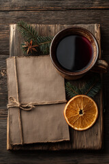 Top view of paper brown blank card tied with twine, mug with mulled wine, fir branches and slice of dried orange on dark wooden background
