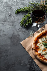 
Top view of Margherita pizza served on craft paper, glass of wine and rosemary branches on grey textured background with space for text
