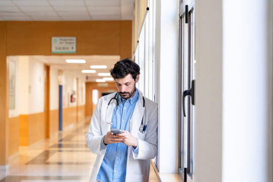 Doctor using smartphone in hospital corridor, reading messages