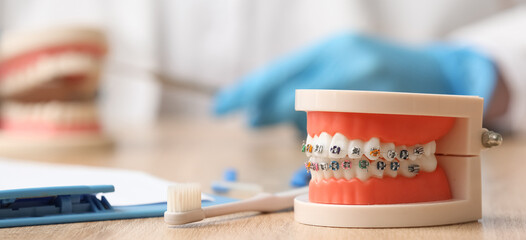 Artificial jaw with toothbrush and clipboard on wooden table, closeup