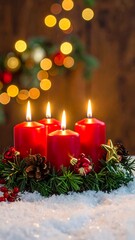 Close-up of four lit red candles in holiday snow and greenery