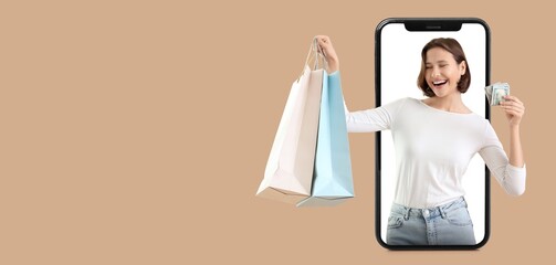 Young woman with money and shopping bags popping out of smartphone screen on beige background with...