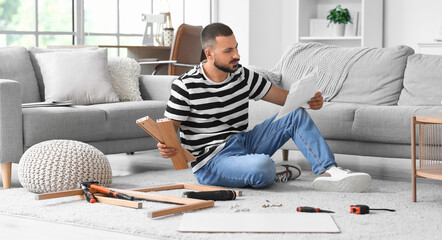 Young man with instructions assembling table at home