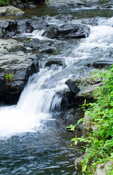 Fresh clear water flowing over black rocks in a tropical forest river near Benang Kelambu waterfall, Lombok, Indonesia. Perfect for nature, relaxation, and travel themes.