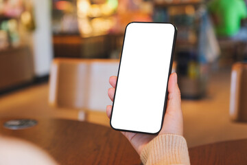 Mockup image of a woman holding and using mobile phone with blank desktop screen in cafe