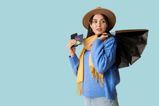 Young woman with shopping bags, credit cards and mobile phone on blue background