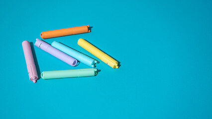 A collection of six minimalist highlighters in soft pastel colors, randomly scattered across a vivid, solid blue background, creating a bright and clean composition.