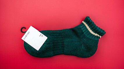 A single, dark green ankle sock with a cream stripe and a blank care label on a vibrant red background.