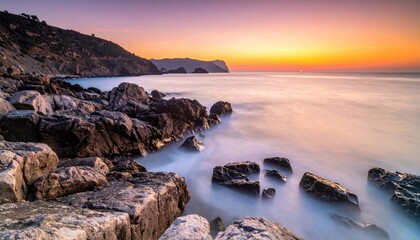 Serene Ocean Sunrise Over Rocky Coastline With Gentle Waves Washing Ashore And Distant Hills Under A Colorful Sky