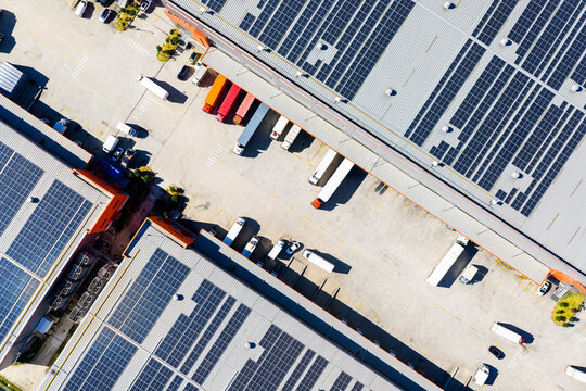 Aerial top view of logistics warehouse with solar rooftops and trucks