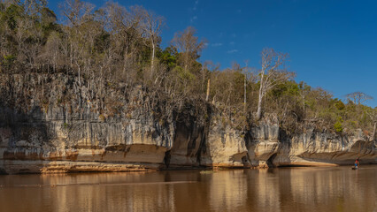 A calm red-brown African river. Trees grow on the steep limestone eroded shores. Reflection on the water. The blue sky. The diagonal. Madagascar. Manambolo river