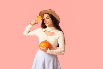 Stylish young woman with fresh pumpkin and autumn leaf on pink background