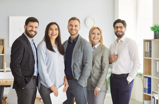 Group of successful business professionals standing together in modern office and looking at camera. Diverse team of smiling colleagues in smart casual outfits showing unity, teamwork and team spirit. - Powered by Adobe