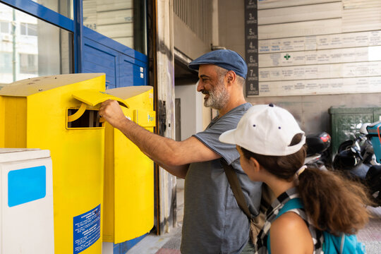 Father and preteen child sending postcards from Athens mailbox