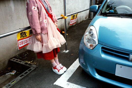 Person in pink bomber jacket, frilly dress and red shoes leans on rail