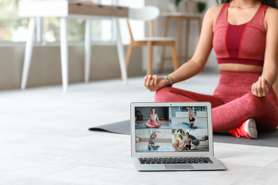 Sporty young African-American female coach with yoga mat and laptop meditating at home. Concept of online training - Powered by Adobe