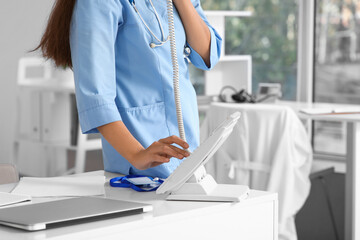 Young female doctor talking by telephone at table in clinic, closeup