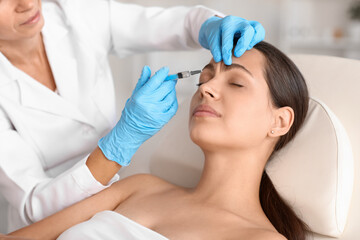 Naklejka premium Young woman receiving forehead filler injection in beauty salon
