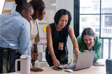 Diverse team collaborates, looking at laptop screen.