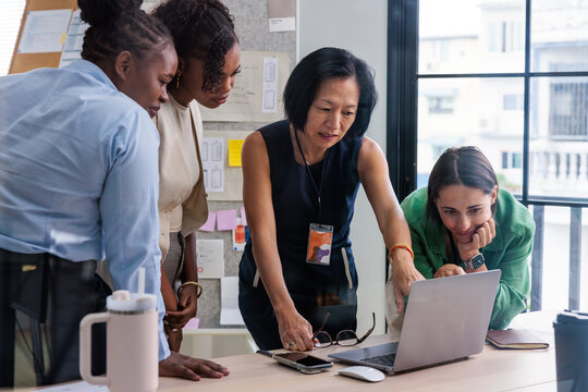 Diverse team collaborates, looking at laptop screen.