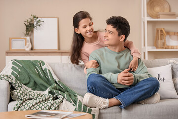 Happy brother and sister hugging while sitting on sofa in living room