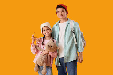 Happy brother and sister showing OK gesture with teddy bear and backpack on yellow background