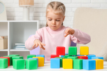 Cute little girl playing with plastic cubes at table in children's room, closeup