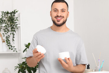 Young man with jar of cream in bathroom