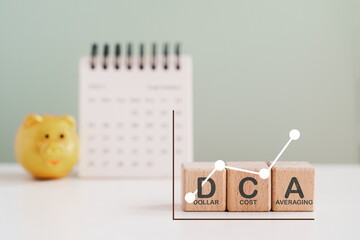 DCA, Dollar Cost Averaging, text on wooden cube block with graph ,blurred calendar and gold piggy bank  background
