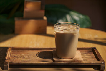 a glass of iced milk coffee on wooden table in sun light and shade