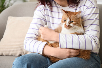 Young woman with cute ginger cat on sofa at home, closeup