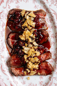 Beef slices with cherry sauce and crispy chips on patterned plate