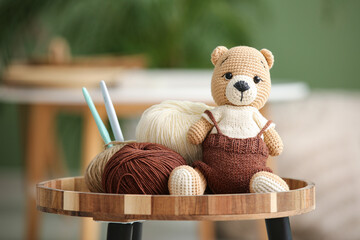 Knitted bear toy with yarn and crochet hooks on coffee table at home